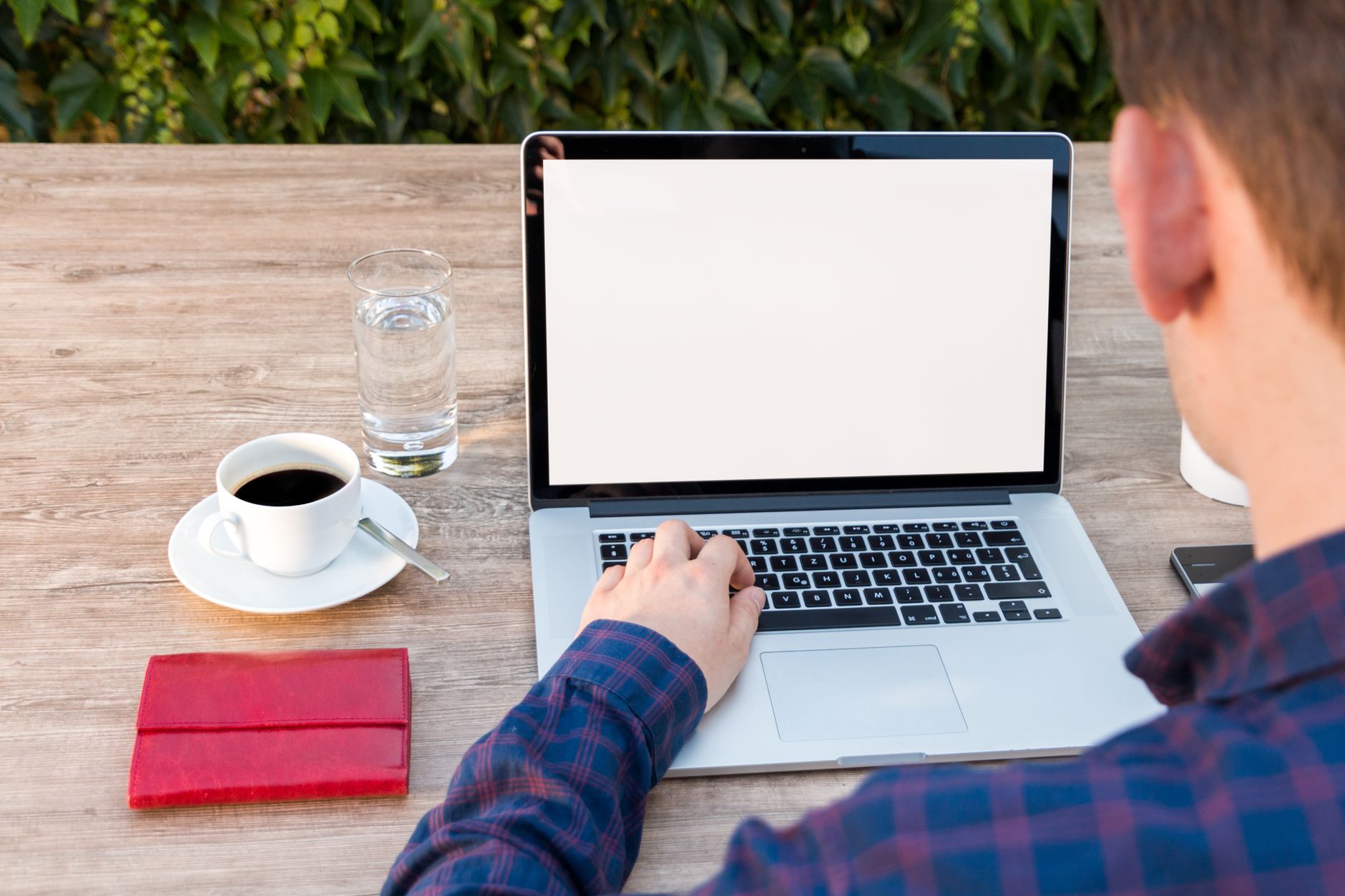 Adulte travaillant sur un ordinateur portable en extérieur avec un café et un bloc-notes, illustrant la flexibilité du travail à distance.